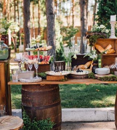 An outdoor reception tablescape with greenery, candles, and tablesettings, including wine barrels as accent decor.